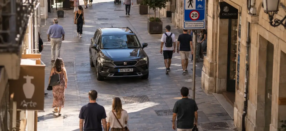 "Qué es una calle de plataforma única" — vista cenital de una calle peatonal-vehicular sin bordillo en un centro urbano español, coche circulando despacio junto a peatones
